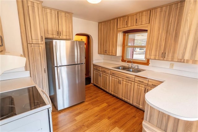 kitchen featuring light wood finished floors, light countertops, freestanding refrigerator, arched walkways, and a sink