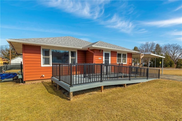 back of property with an attached carport, fence, a wooden deck, roof with shingles, and a yard