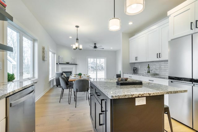 kitchen with light wood finished floors, backsplash, appliances with stainless steel finishes, hanging light fixtures, and white cabinets