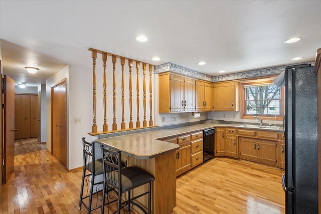 kitchen featuring a breakfast bar area, a peninsula, a sink, black appliances, and light wood-type flooring