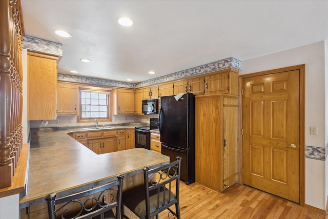 kitchen with a sink, light wood-type flooring, black appliances, and recessed lighting