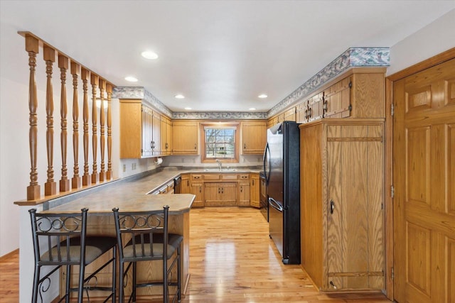 kitchen with a sink, a peninsula, light wood-style flooring, and freestanding refrigerator