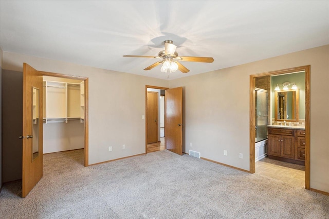 unfurnished bedroom featuring a walk in closet, light colored carpet, visible vents, and baseboards