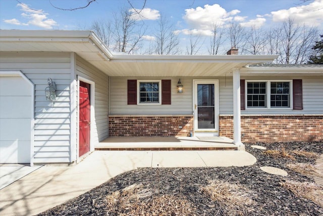 entrance to property with a garage, covered porch, brick siding, and a chimney