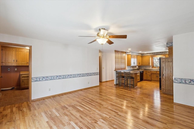 kitchen featuring a kitchen bar, a ceiling fan, brown cabinetry, light wood finished floors, and dishwasher