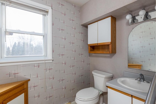 bathroom with vanity, toilet, and wallpapered walls