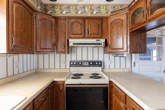 kitchen with electric range oven, decorative backsplash, light countertops, under cabinet range hood, and brown cabinets