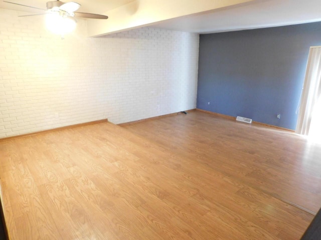 empty room featuring a ceiling fan, wood finished floors, visible vents, brick wall, and beamed ceiling