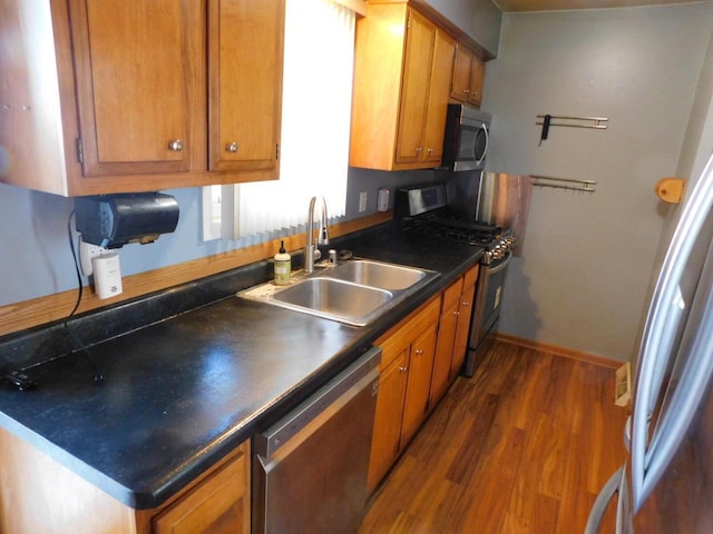 kitchen featuring dark countertops, dark wood finished floors, brown cabinetry, stainless steel appliances, and a sink