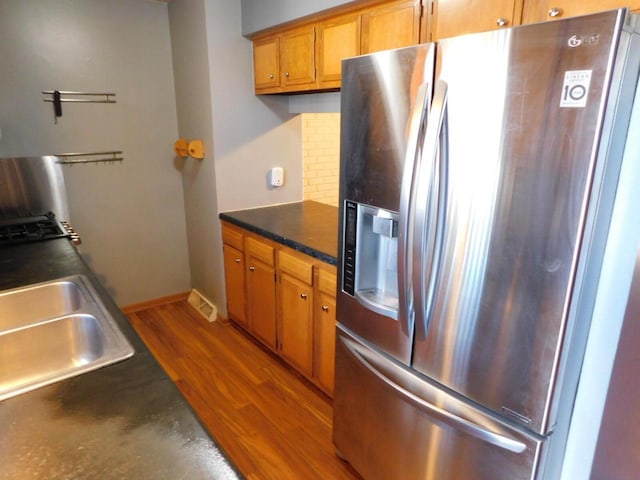 kitchen featuring stainless steel refrigerator with ice dispenser, dark countertops, wood finished floors, brown cabinetry, and decorative backsplash