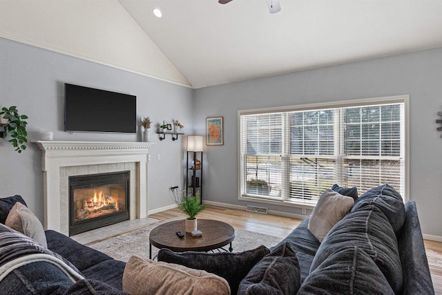 living room featuring a tiled fireplace, baseboards, a ceiling fan, and wood finished floors