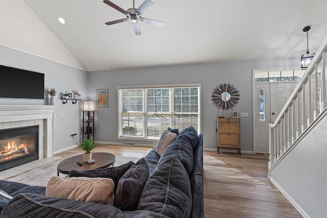 living room featuring wood finished floors, baseboards, ceiling fan, stairs, and a tiled fireplace