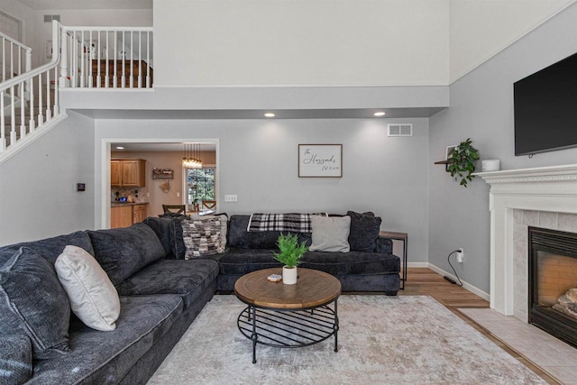 living area with visible vents, baseboards, stairway, a tile fireplace, and a high ceiling