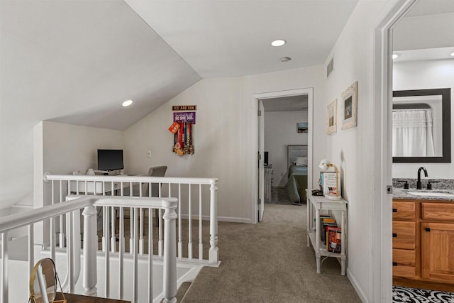 corridor with visible vents, a sink, vaulted ceiling, an upstairs landing, and light colored carpet