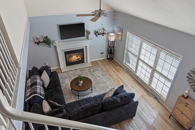 living area featuring wood finished floors, visible vents, lofted ceiling, a fireplace with flush hearth, and ceiling fan