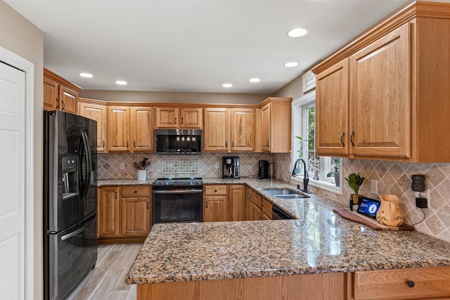 kitchen featuring light stone countertops, a peninsula, light wood-style floors, black appliances, and a sink