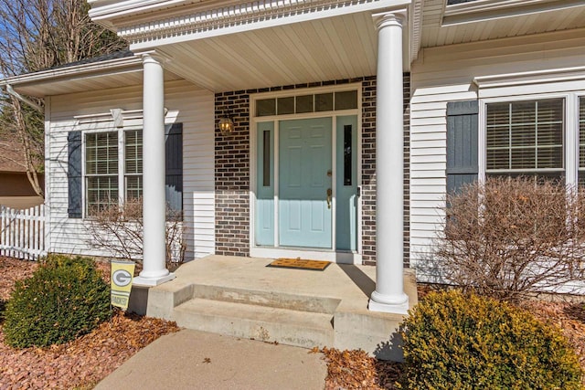 property entrance featuring brick siding, a porch, and fence