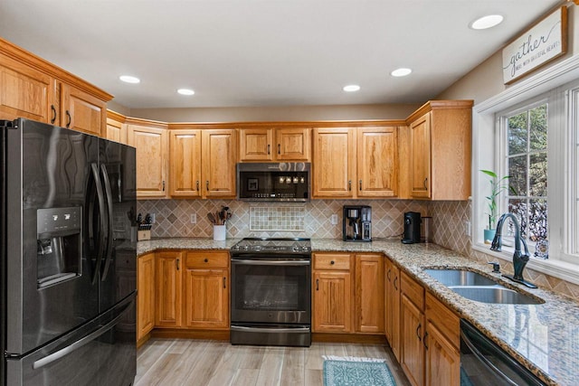 kitchen featuring black appliances, a sink, light stone counters, backsplash, and light wood finished floors