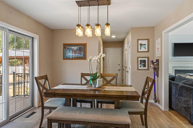 dining space featuring light wood-style flooring, visible vents, baseboards, and a tile fireplace