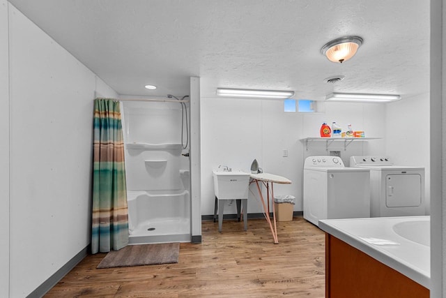 full bathroom featuring washing machine and clothes dryer, a shower stall, a textured ceiling, and wood finished floors