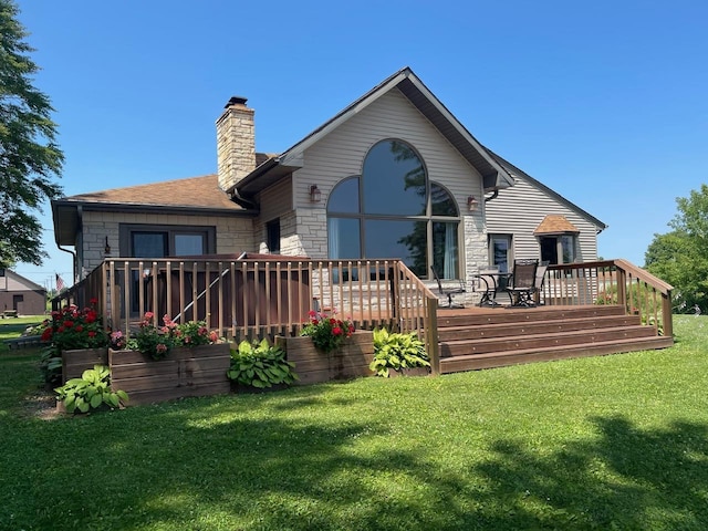 back of house featuring a wooden deck, a yard, a shingled roof, a chimney, and stone siding