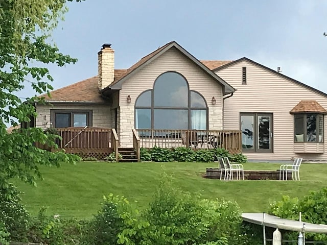 back of house with a yard, stone siding, a wooden deck, and a chimney