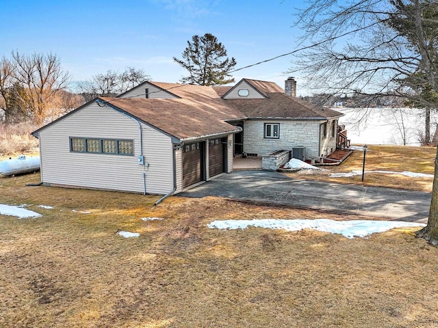 view of front facade featuring central AC unit, a shingled roof, a chimney, a garage, and aphalt driveway