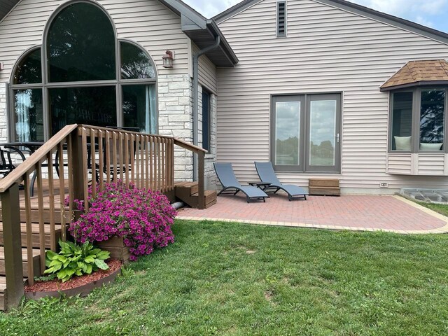 rear view of house featuring a patio area, stone siding, and a yard