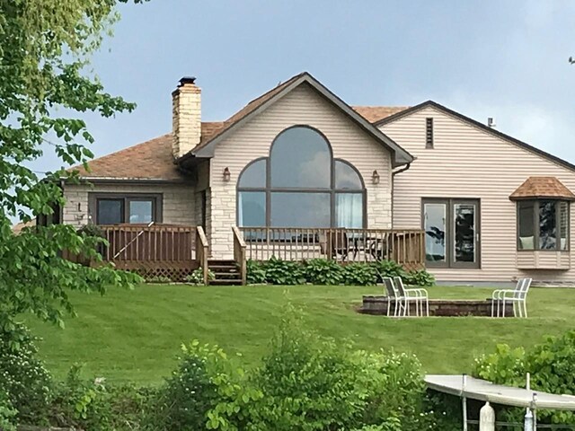 back of property with a deck, a lawn, stone siding, and a chimney