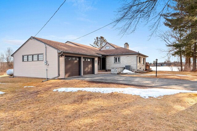 view of front facade with central AC unit, a chimney, a garage, stone siding, and driveway