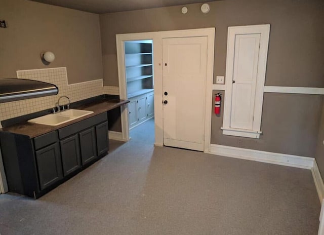 kitchen with a sink, dark countertops, tasteful backsplash, carpet floors, and baseboards