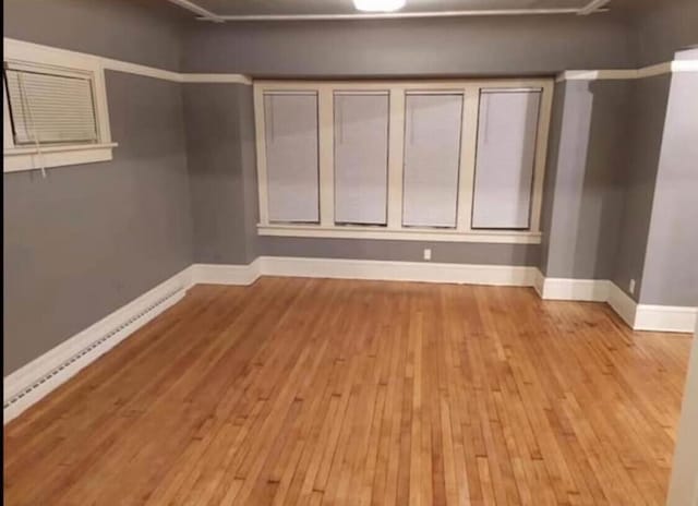 empty room with a baseboard heating unit, wood finished floors, and baseboards