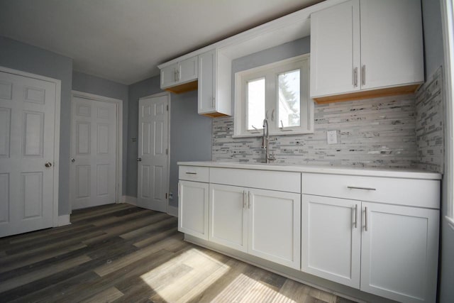 kitchen featuring backsplash, light countertops, wood finished floors, white cabinetry, and a sink