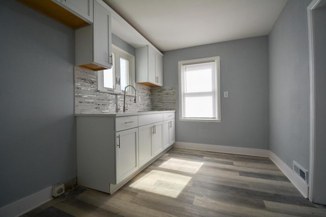 kitchen featuring baseboards, light wood-style flooring, a sink, decorative backsplash, and light countertops