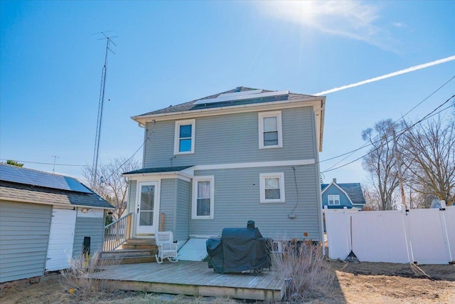 back of property featuring a deck, fence, and roof mounted solar panels