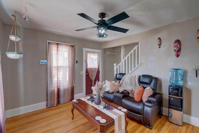 living area featuring ceiling fan, stairway, baseboards, and light wood-style flooring