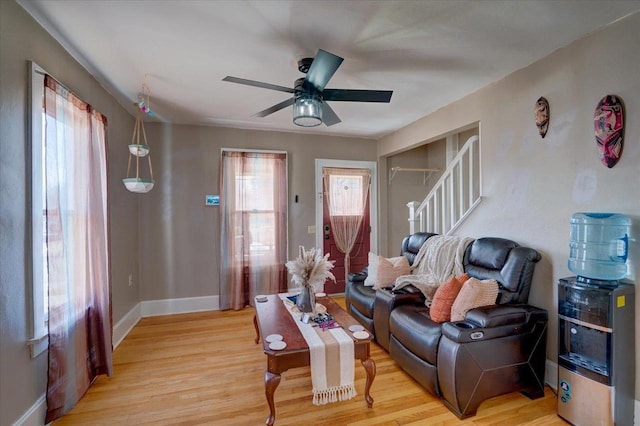 living area with baseboards, stairs, light wood-type flooring, and a ceiling fan