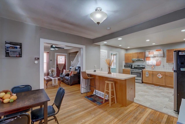 kitchen with under cabinet range hood, a peninsula, appliances with stainless steel finishes, a breakfast bar area, and light wood finished floors