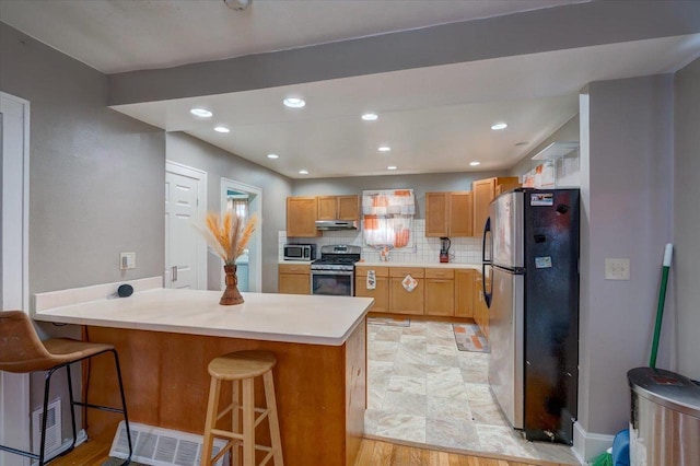 kitchen featuring under cabinet range hood, a kitchen breakfast bar, backsplash, appliances with stainless steel finishes, and a peninsula