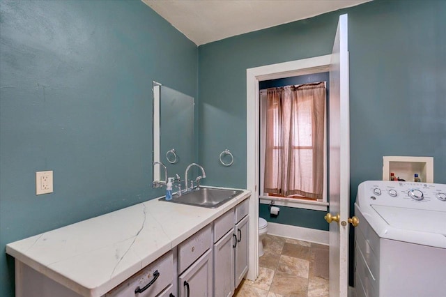 washroom with stone finish flooring, baseboards, laundry area, washer / dryer, and a sink