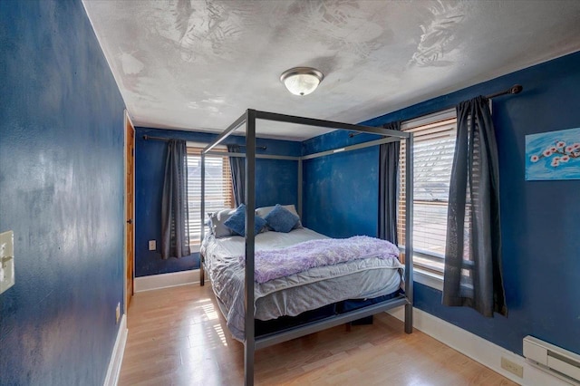 bedroom with a textured ceiling, a baseboard heating unit, baseboards, and wood finished floors