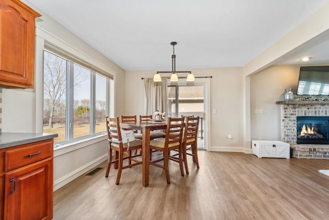 dining space featuring visible vents, baseboards, a brick fireplace, and light wood-style flooring