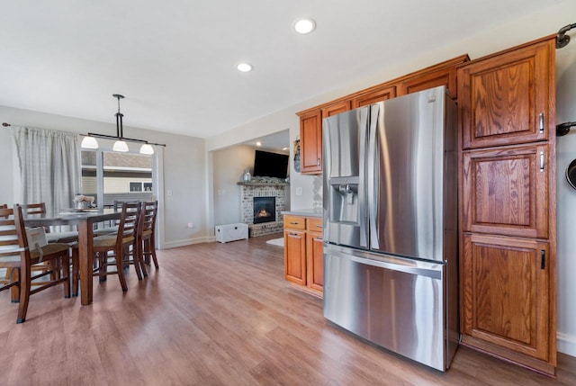 kitchen featuring brown cabinetry, stainless steel fridge, a fireplace, and light wood-style floors