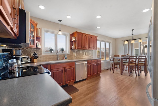 kitchen with light wood finished floors, glass insert cabinets, decorative backsplash, stainless steel dishwasher, and a sink