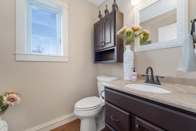 half bath with baseboards, toilet, wood finished floors, and vanity