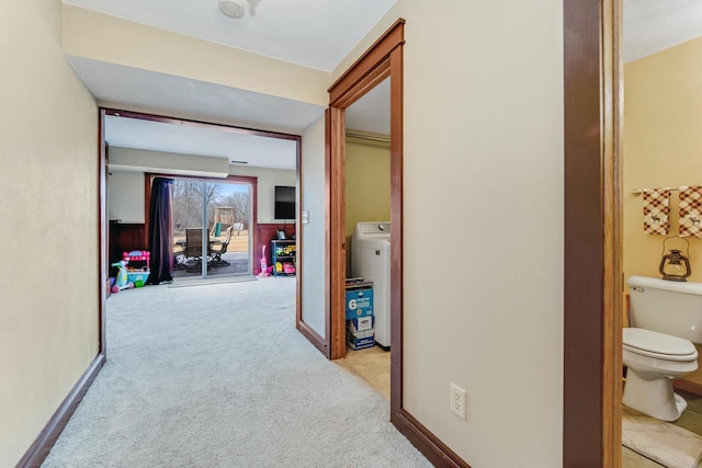 corridor featuring washer / clothes dryer, baseboards, and light carpet