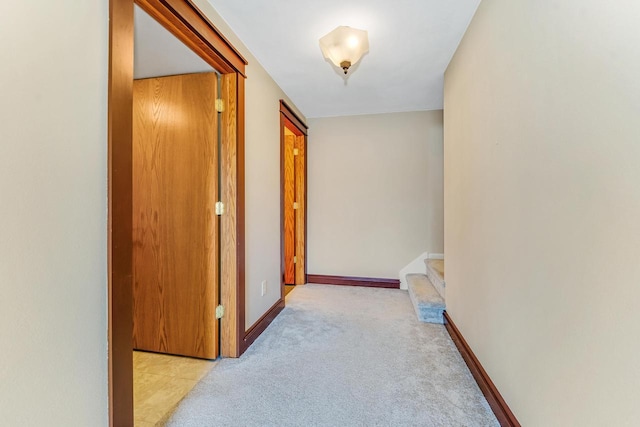 hall featuring stairs, baseboards, and light carpet