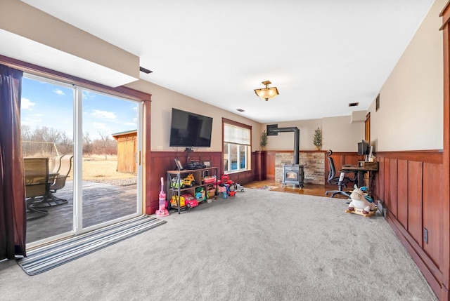 playroom featuring a wainscoted wall, carpet flooring, and a wood stove