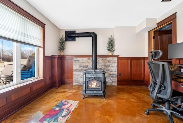 office with a wood stove, wooden walls, concrete floors, and wainscoting