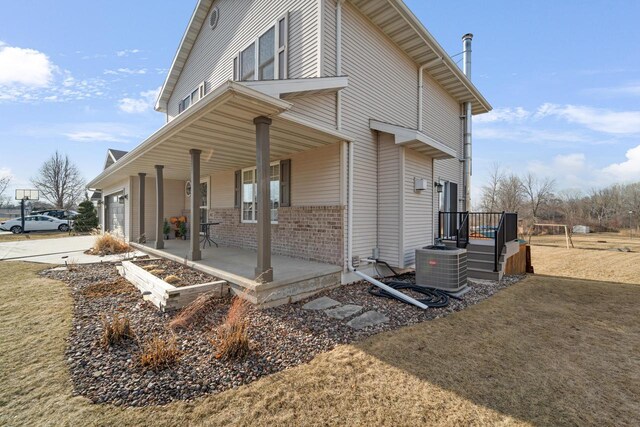 view of side of property with a porch, concrete driveway, a garage, brick siding, and central AC unit